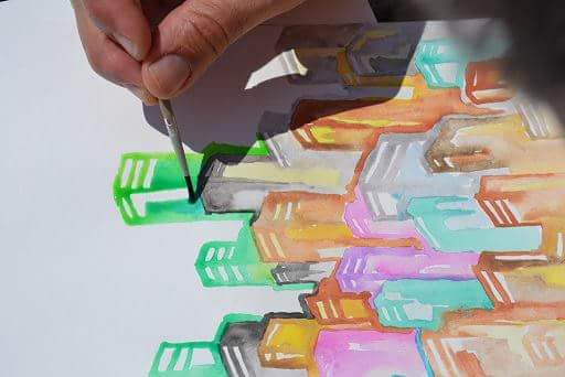 Una mano dipinge con un pennello le forme colorate di una città